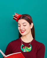 Jolly Granny Dino-Claus reading to her Grand-Elf-Dinos Necklace